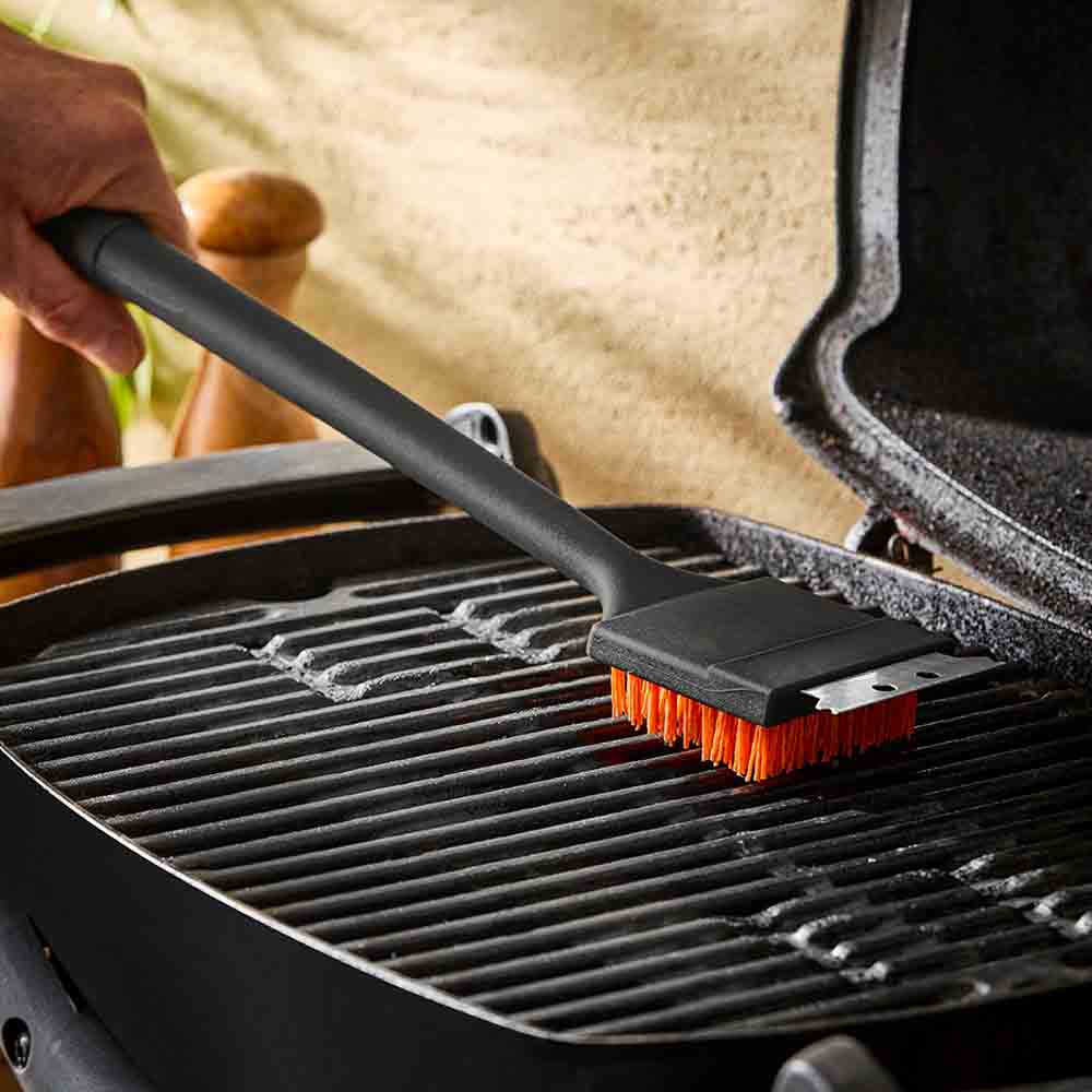 man cleaning BBQ with long handled grill brush - Robins Kitchen
