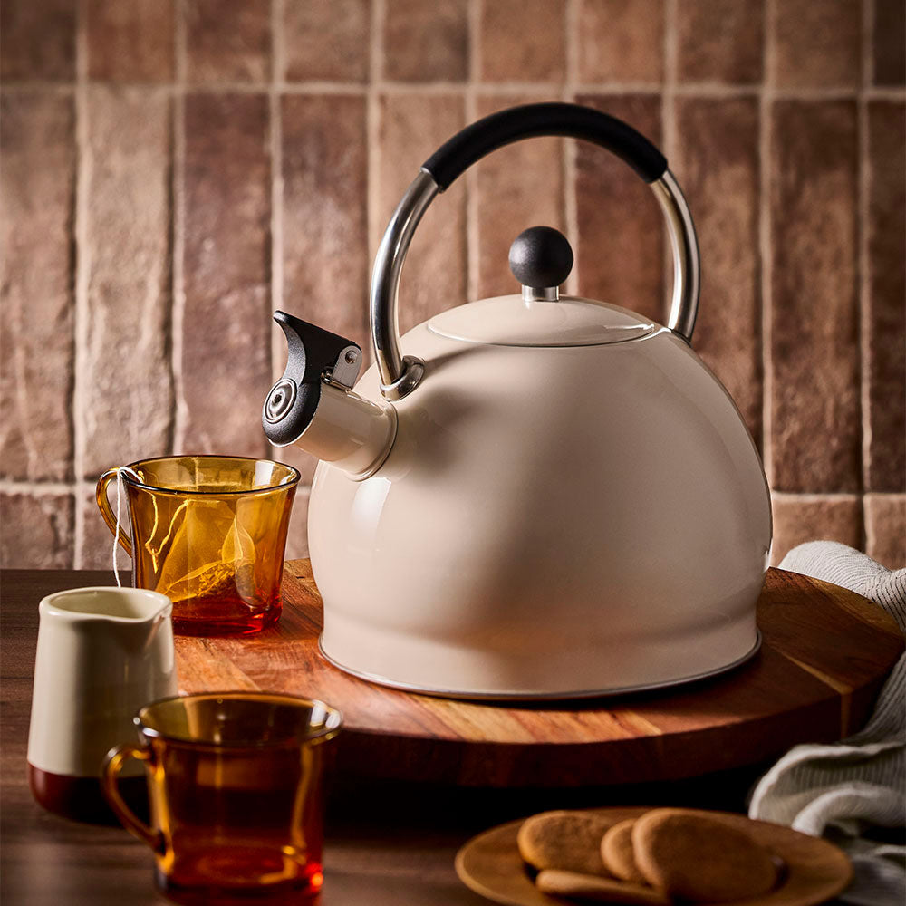 Stovetop kettle in oat displayed beside a teacup with a dry tea bag inside.