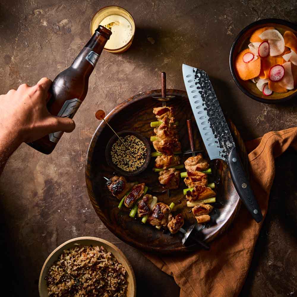 Man pouring beer beside Baccarat KUROI KIBA Santoku Knife 18cm at Robins Kitchen