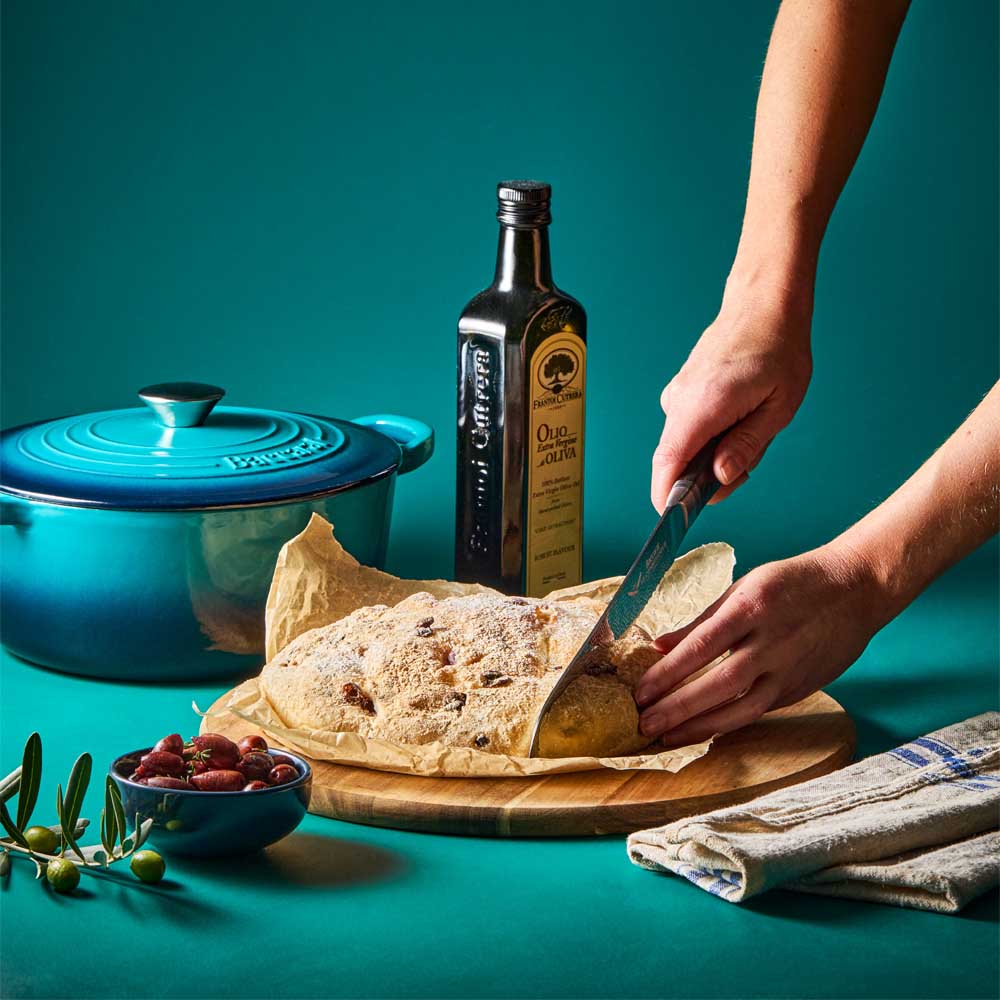 woman cutting bread baked from blue french oven - Robins Kitchen